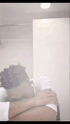 a man in a white shirt is covering his face in a bathroom