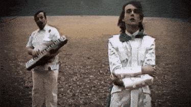 a man in a white suit is playing a keyboard while another man in a white suit is standing next to him