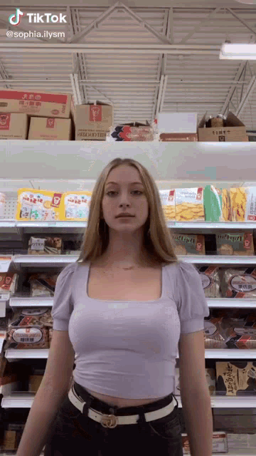 a woman in a purple crop top is standing in front of a grocery shelf .