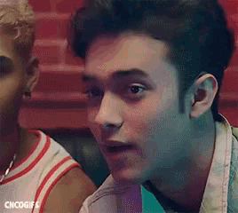 a young man is making a funny face while sitting next to another young man in a restaurant .