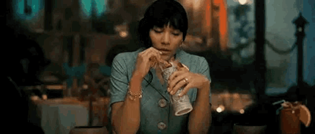a woman is sitting at a table in a restaurant eating a sandwich and drinking from a cup .