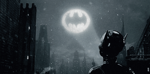 a man in a batman suit stands in front of a large batman logo