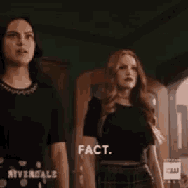 two women are standing next to each other in a room and one of them is saying fact .