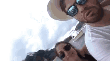 a man and a woman wearing sunglasses and a hat are taking a picture of themselves .