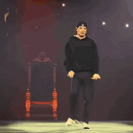 a man in an orange shirt is dancing on a stage with fire coming out of his hands .