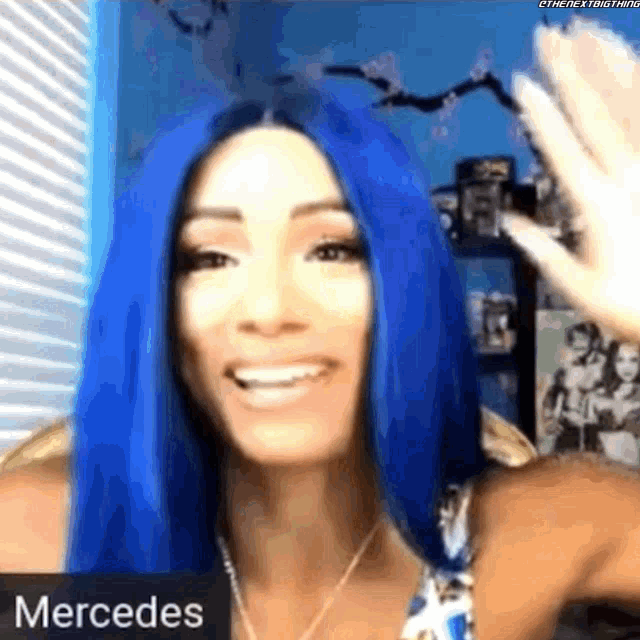 a woman with blue hair is smiling and waving while wearing a mercedes shirt .