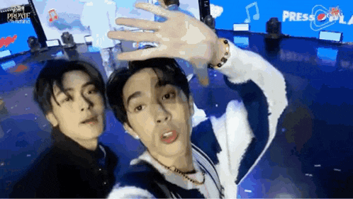 two young men are posing for a picture in front of a blue screen that says press play .