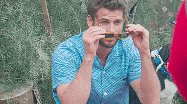 a man wearing a blue shirt and sunglasses is sitting on a chair .