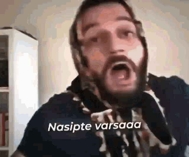 a man with a beard and scarf around his neck is making a funny face with his mouth open .