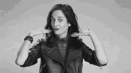 a woman in a leather jacket is holding her hair in her hands in a black and white photo .