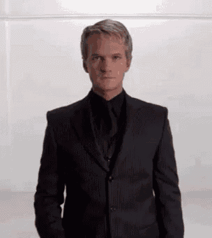 a man in a suit and tie is standing in a room with his hands in his pockets .