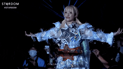 a woman in a white dress stands in front of a crowd and the word stardom is on the bottom right