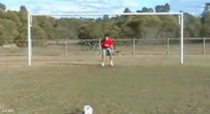 a man in a red shirt is kicking a soccer ball in front of a goal