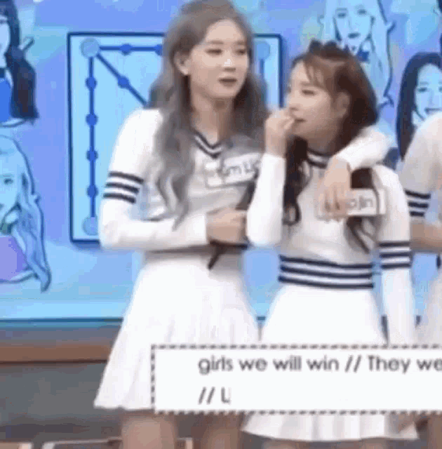 two girls are standing next to each other on a stage and one of them is covering her mouth with her hand .