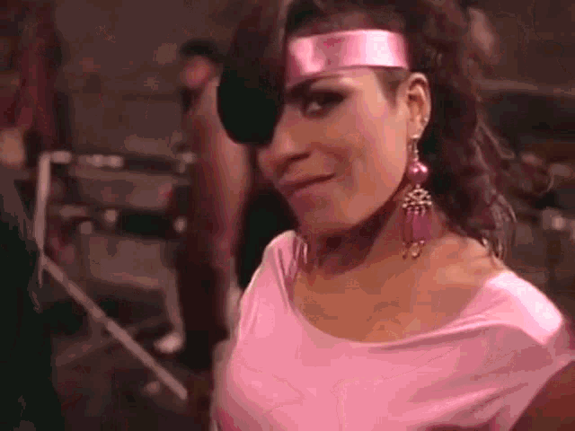 a woman wearing a pink headband and earrings is smiling and looking at the camera .