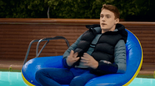 a man in a black vest is sitting in a blue raft in a pool