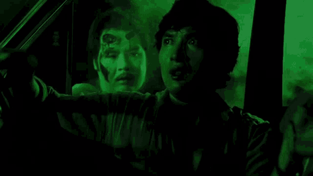 a man is driving a car in a dark room with a ghost behind him .