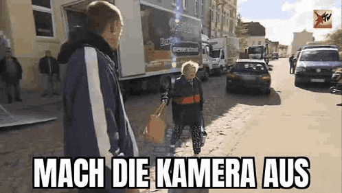 a man and a child are walking down a street in front of a truck and a sign that says mach die kamera aus .
