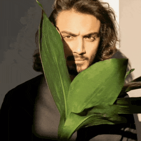 a man with long hair and a beard is holding a green plant in front of his face