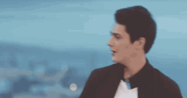 a man in a tuxedo is standing in front of a body of water and looking at the camera .
