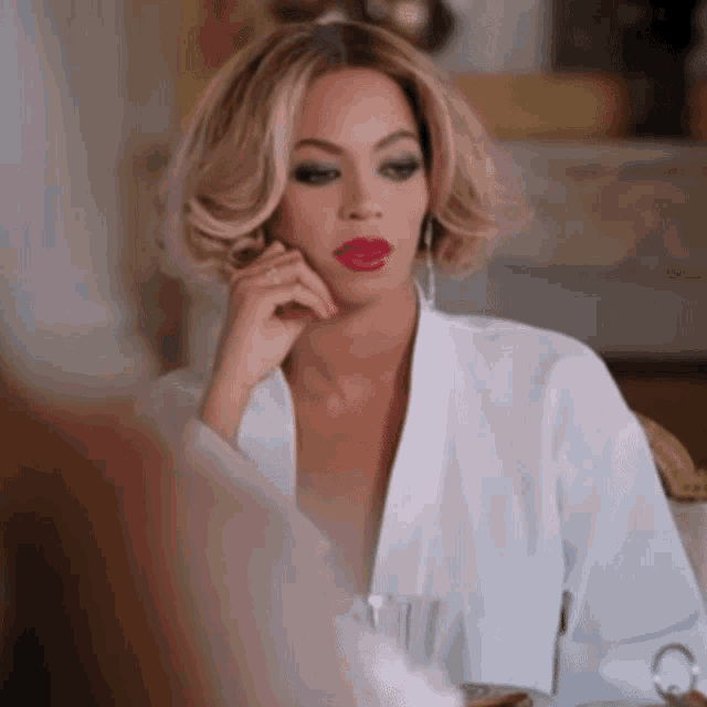 a woman wearing red lipstick and a white shirt is sitting at a table
