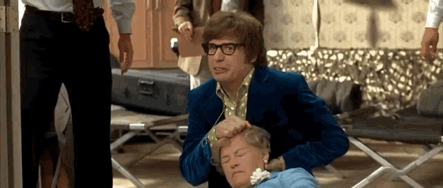 a man in a blue suit and glasses is putting his hand on a woman 's head