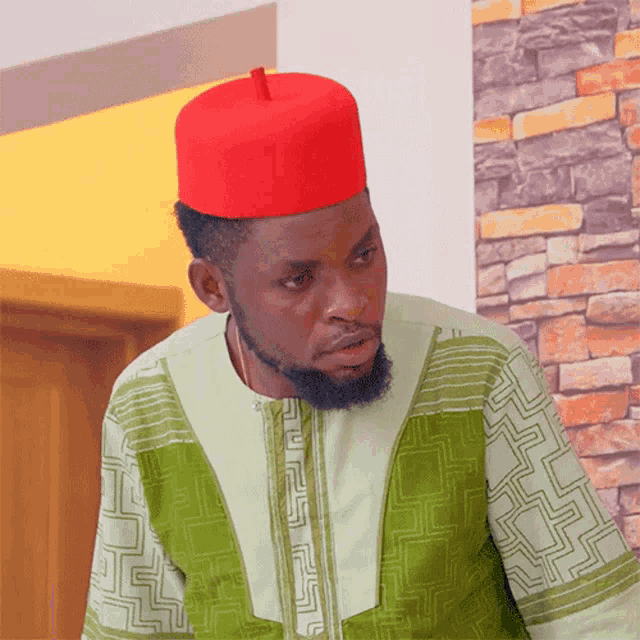 a man wearing a green shirt and a red hat looks at the camera