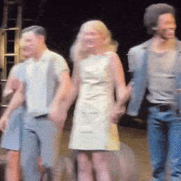 a woman in a white dress holds hands with two men on a stage