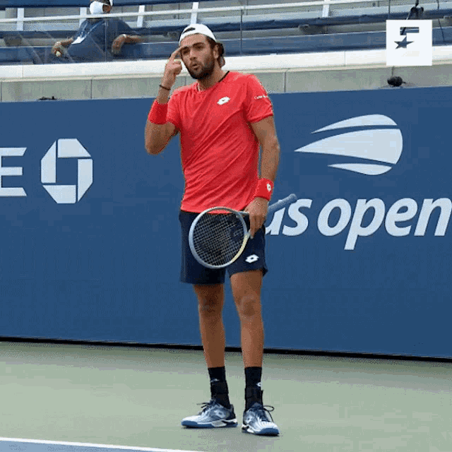 a man in a red shirt holds a tennis racquet in front of a sign that says us open