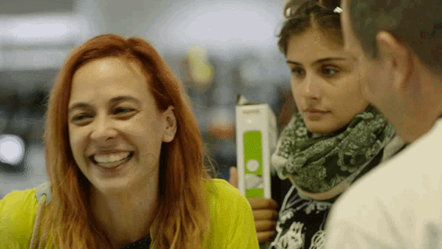 a woman in a yellow shirt is smiling while holding a box that says ' i 'm sorry ' on it