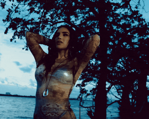 a woman stands in front of a body of water and trees
