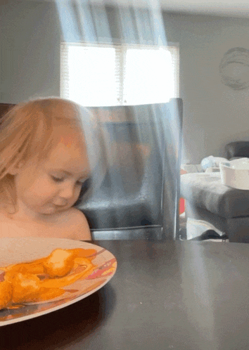a little girl looking at a plate of food on a table