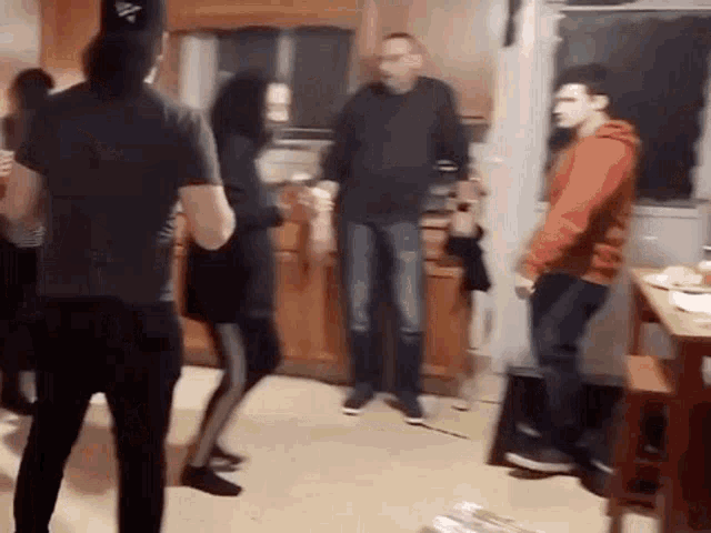 a group of people are dancing in a kitchen while a man stands in the background .