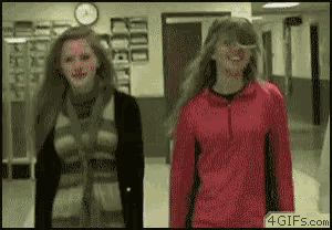 two girls are walking down a hallway with a clock on the wall behind them .
