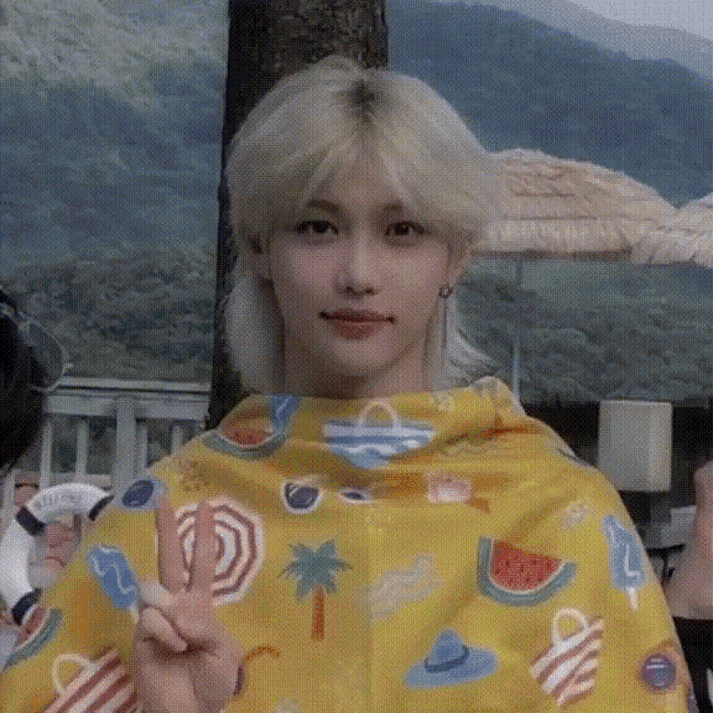 a young man wearing a yellow blanket is giving the peace sign .