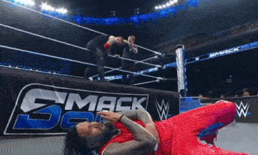 a wrestler in a red outfit is laying on the ground in front of a smackdown sign