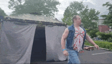 a man wearing a tie dye shirt and a denim vest is walking towards a tent .