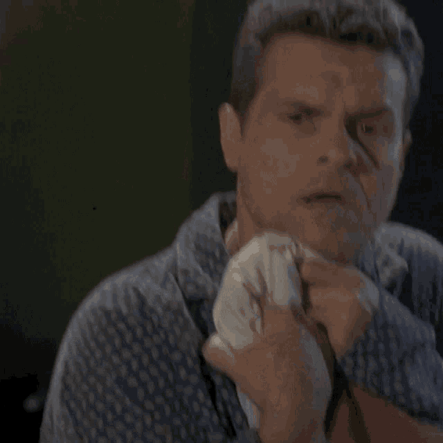 a man in a blue and white polka dot shirt wipes his face with a napkin