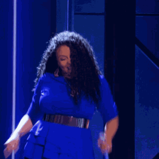 a woman in a blue dress and gold belt is dancing on a stage