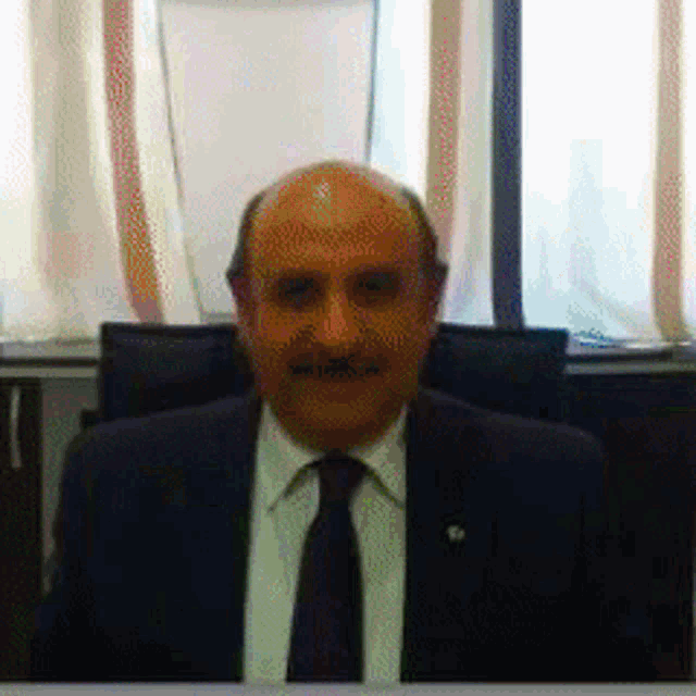 a bald man wearing a suit and tie looks at the camera