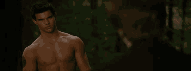 a shirtless man is standing next to a woman in a forest