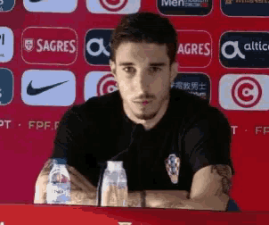 a man is sitting at a table with bottles of water in front of a sign that says sagres
