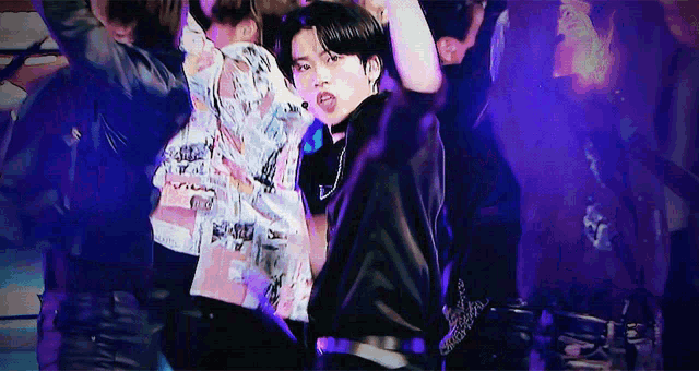 a man in a black jacket is dancing on a stage with a group of people behind him .