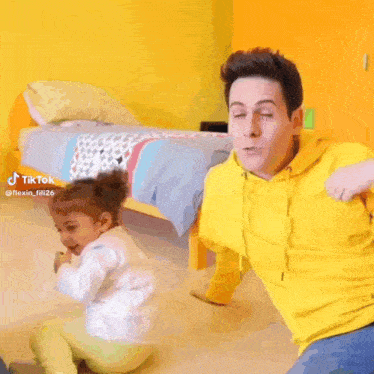 a man in a yellow hoodie playing with a little girl