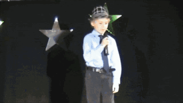 a young boy singing into a microphone wearing a hat
