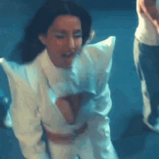 a woman in a white dress is dancing in a dark room with a man standing behind her .