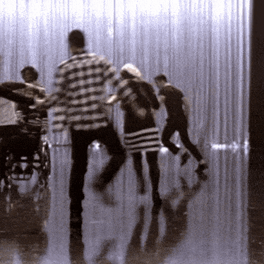 a group of people are dancing in a room with a curtain behind them