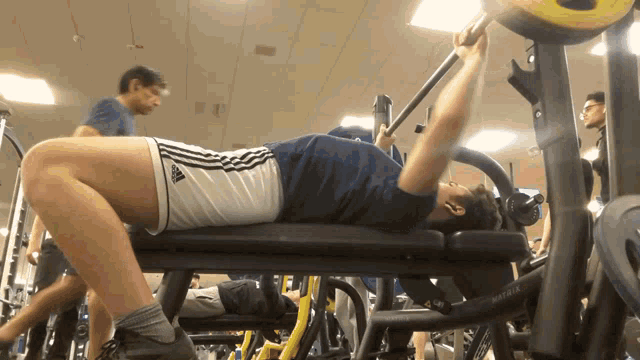 a man is laying on a bench lifting a barbell and his shorts say adidas on the side