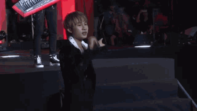 a man in a suit is standing on a stage in front of a crowd and giving a thumbs up .