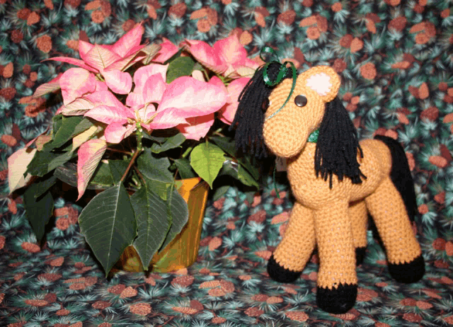 a crocheted horse is sitting next to a potted plant